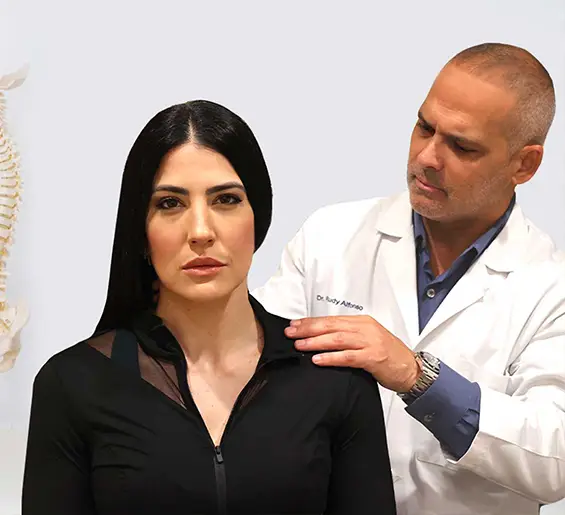 Dr. Rudy Alfonso performing a chiropractic shoulder assessment on a female patient at Sunset Chiropractic & Wellness. A spine model is visible in the background