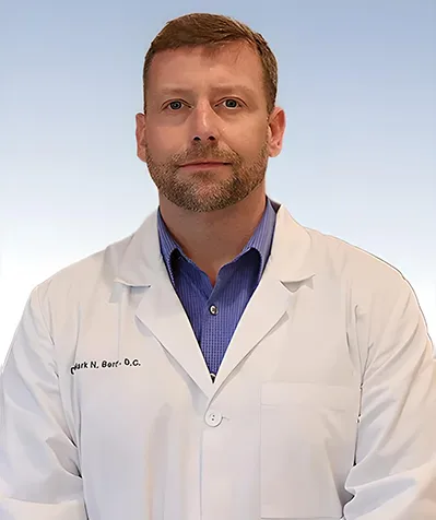 Dr. Mark N. Berry, D.C., wearing a white lab coat and blue shirt, posing with a neutral expression against a light blue gradient background.