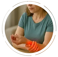 Middle-aged woman sitting at a desk, holding her painful wrist with a red glow indicating carpal tunnel syndrome, while a laptop is open in front of her.