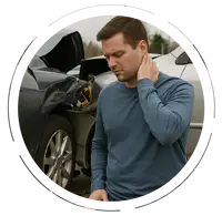 Man kneeling on the ground and holding his neck in pain after a car accident, with two damaged vehicles behind him on a suburban street.