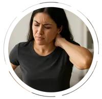 Young woman with long dark hair holding her neck and lower back in pain, showing signs of chronic neck and back discomfort in a softly lit home environment.